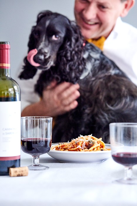 Lifestyle fotografie hond kijkt likkebaardend naar bord met pasta